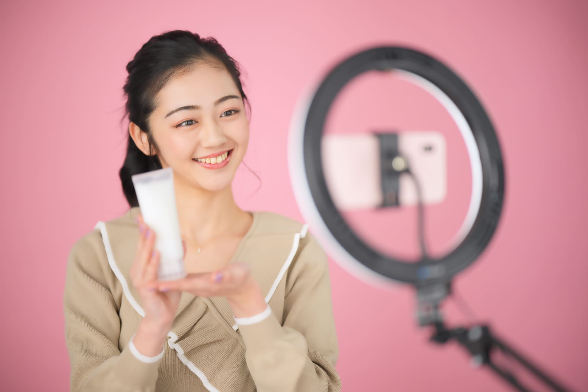 女性がライトとスマートフォンの前でスキンケア用品を手に持っています