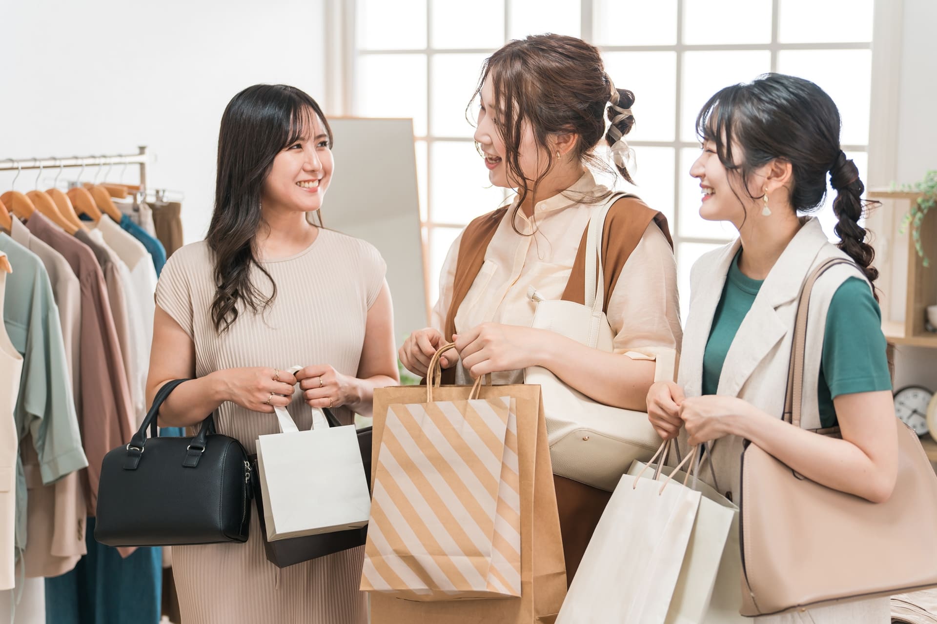 紙袋を持った三人の女性が洋服店で会話をしています